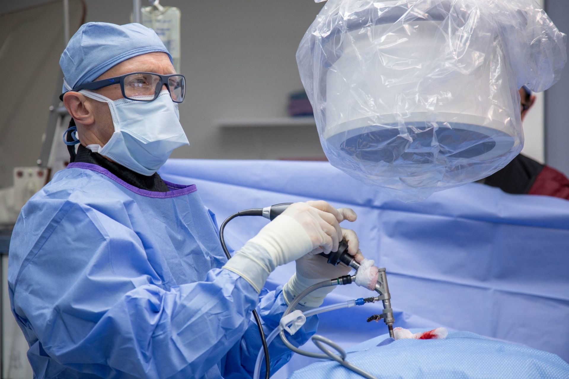 A Surgeon Wearing Glasses And A Mask Is Operating On A Patient
