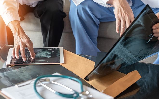 Two Doctors Are Looking At An X-Ray On A Tablet