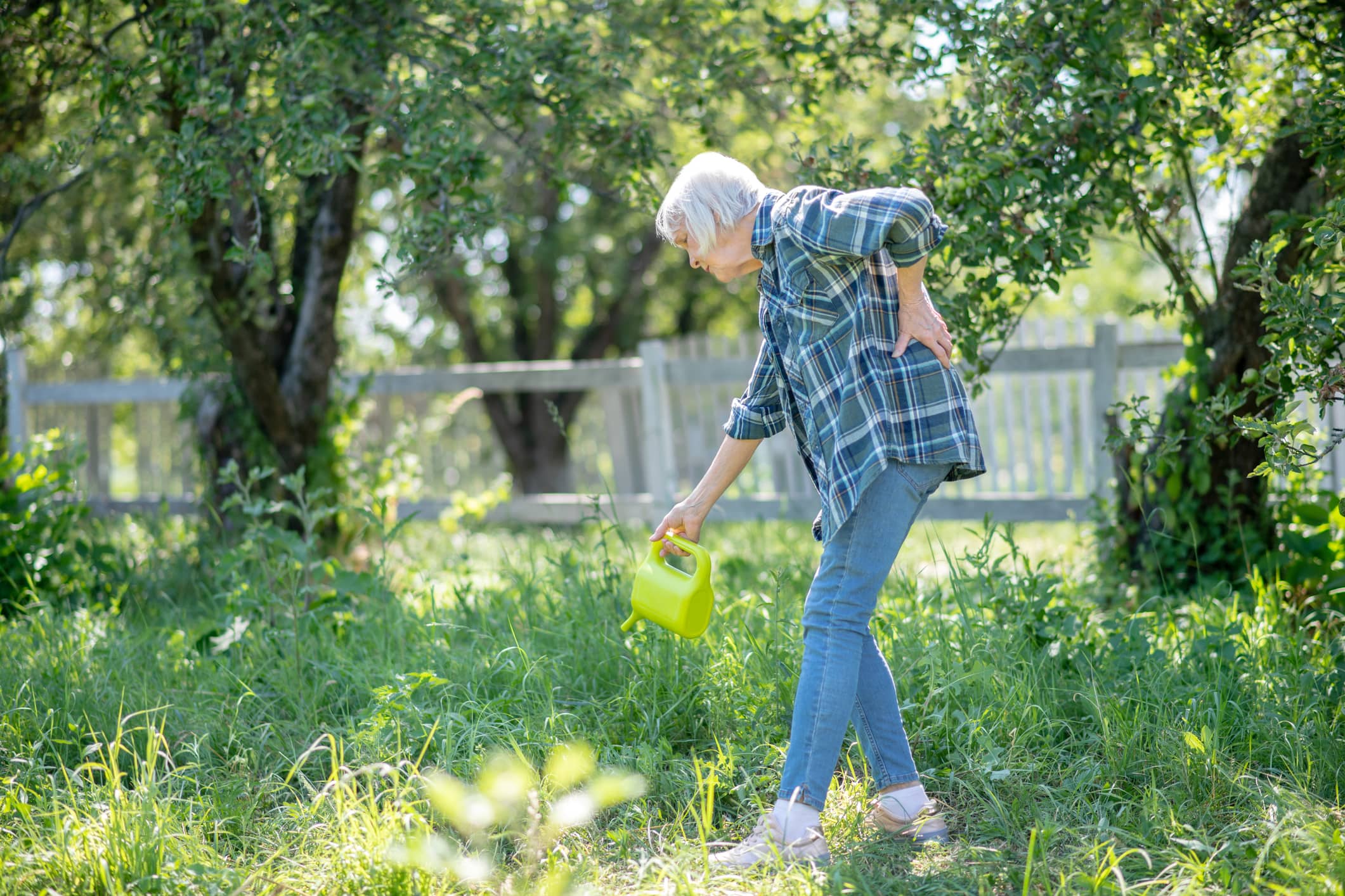 A Woman Bent Over In The Grass Holding A Green Watering Can